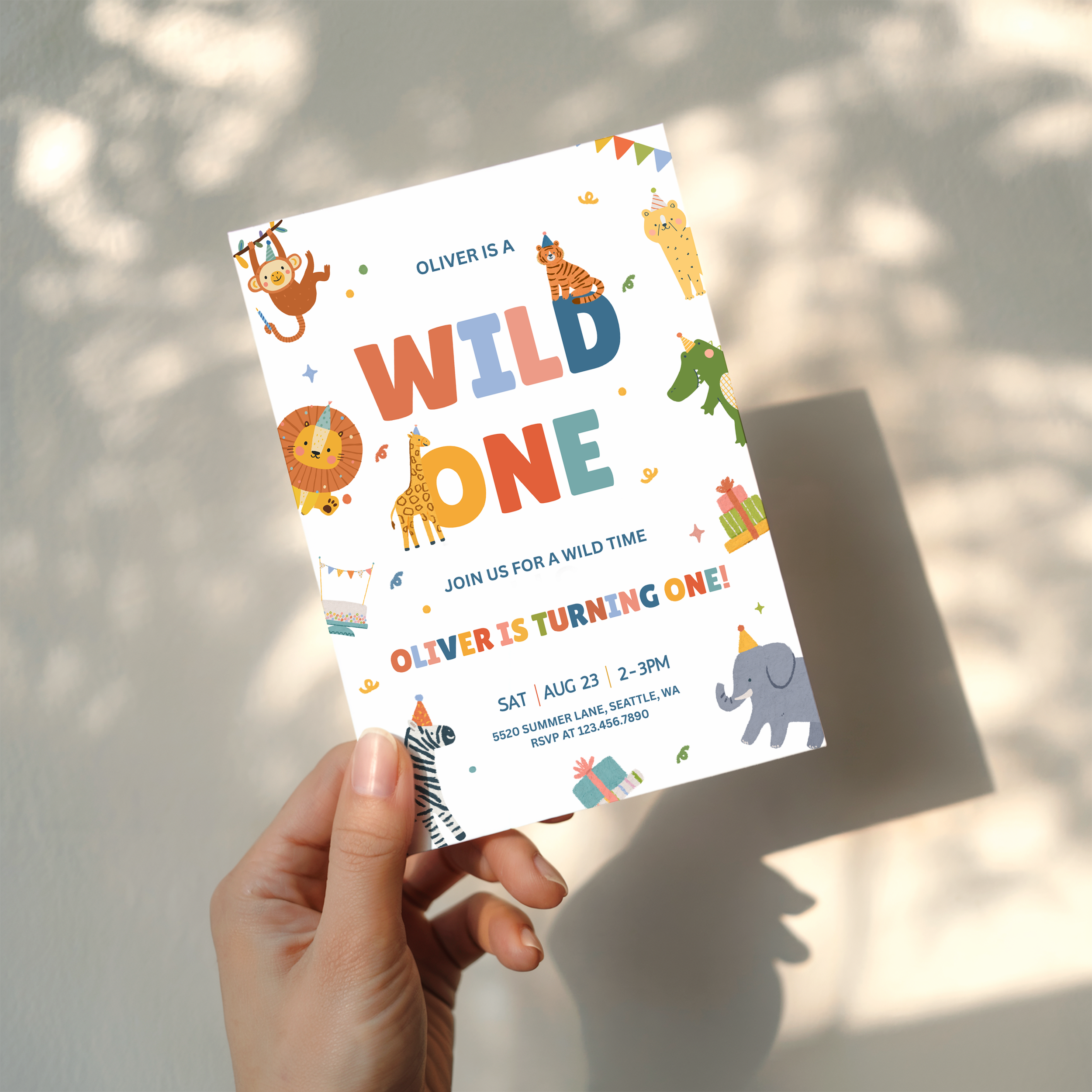 Hand holding a colorful 'Wild One' birthday invitation card with animal illustrations.